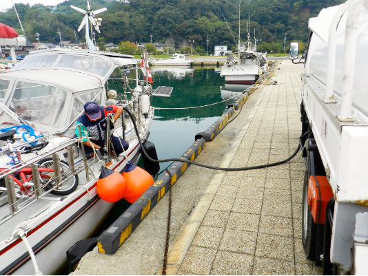 A photo of a man serving fuel from the fuel track to a yacht in fishing port