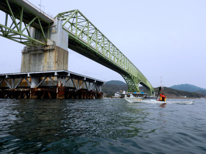 A photo of a person kayaking under an iron bridge